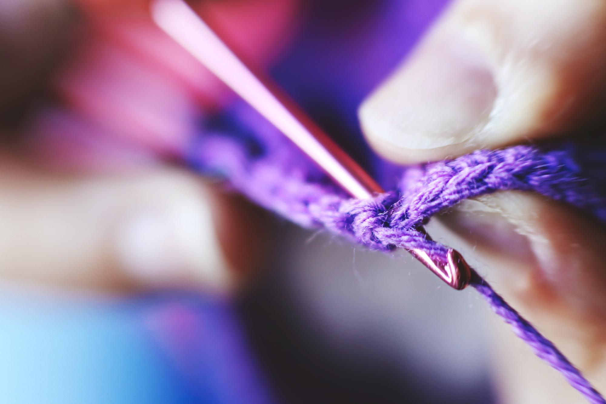 Close-up of hands embroidering neon thread on dark fabric